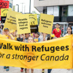 People carrying the Walk with Refugees banner and signs