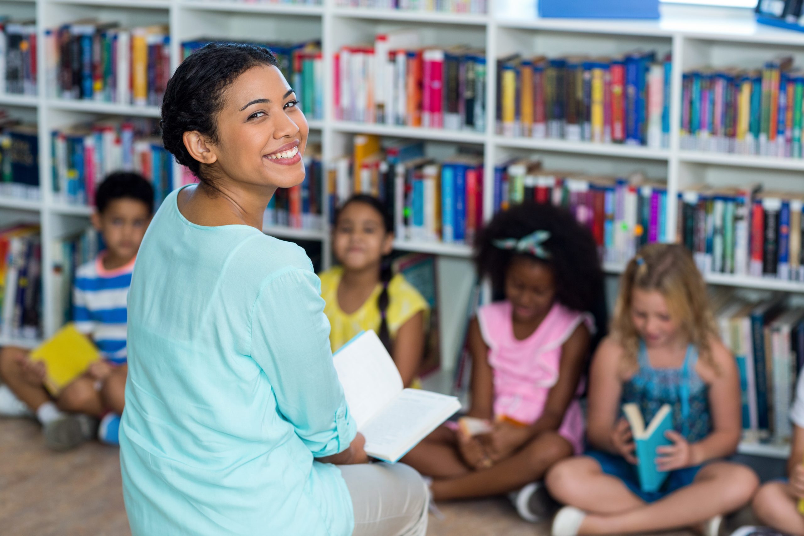A teacher smiling with children who are reading books