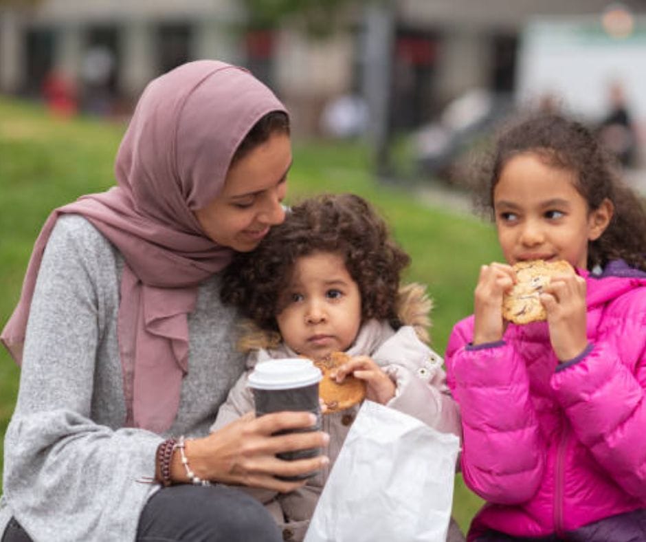 Newcomers (a woman and 2 kids) eating in the park.