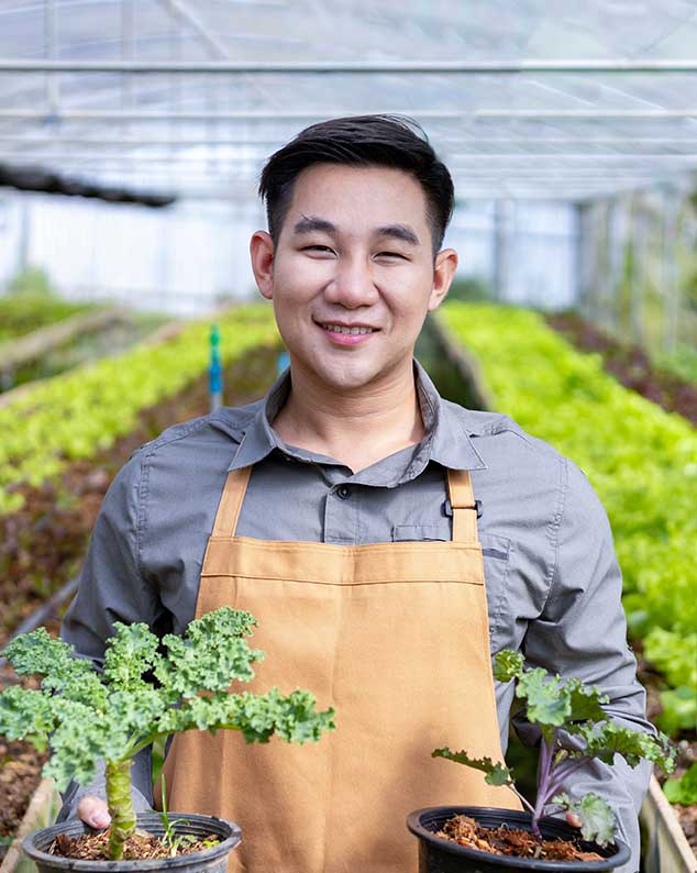 Smiling immigrant male holding plants in a garden