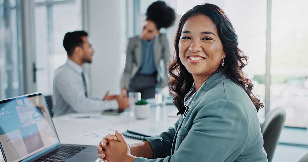 An internationally recruited employee smiling in the office in front of her laptop