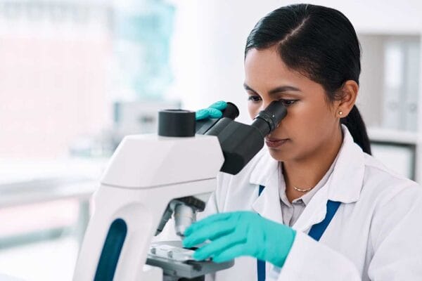 An internationally educated female healthcare professional working in a laboratory looking through a microscope