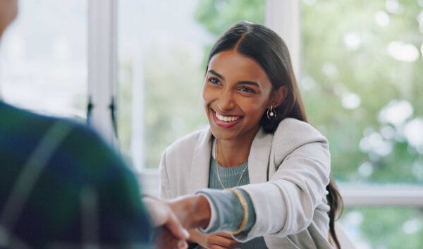 A female newcomer smiling and wearing business attire while shaking hands with an employer