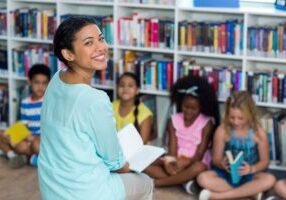 A teacher smiling with children who are reading books