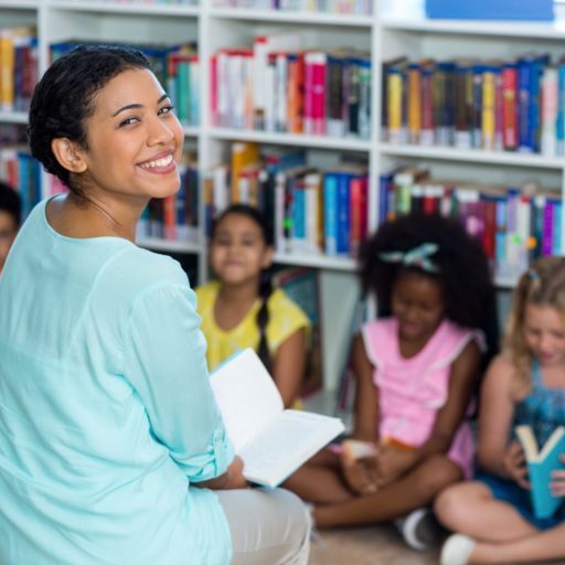 A teacher smiling with children who are reading books