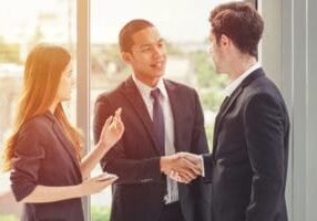 An immigrant youth wearing a suit and shaking hands with co-worker