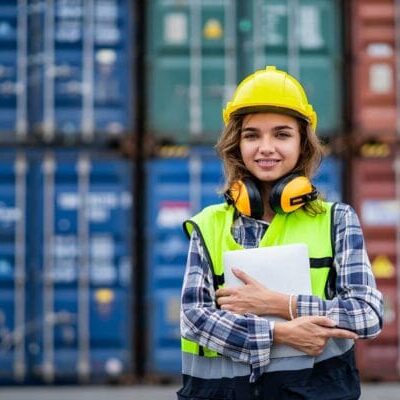 A woman worker wearing protective gear in front of shipping containers