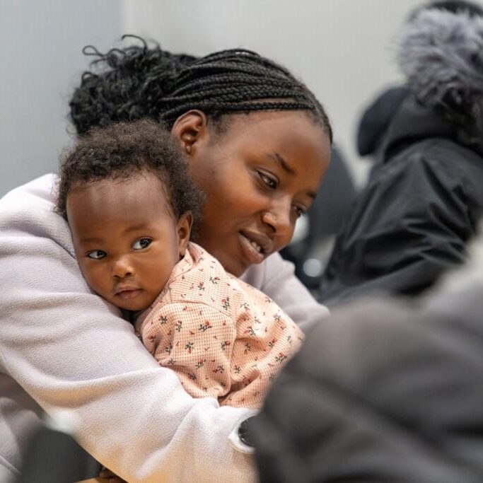 Mother with braided hair tenderly holding her baby, both looking downward.