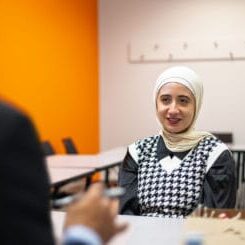 Woman in a hijab smiling, seated at a table during a job interview.