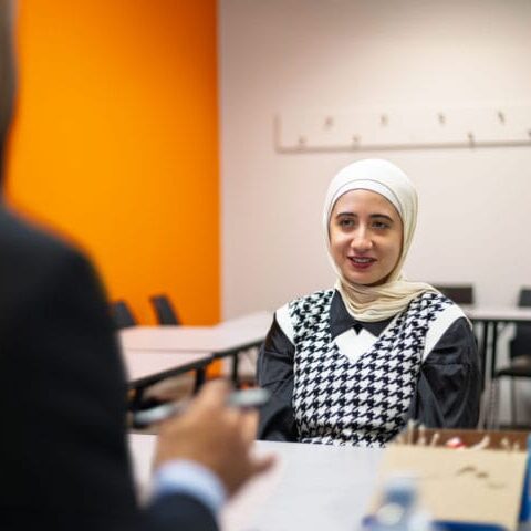 Woman in a hijab smiling, seated at a table during a job interview.