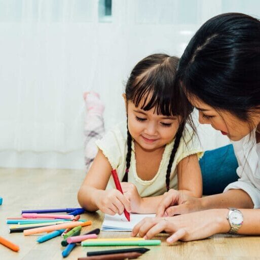A parent woman teaching her daughter to write/draw