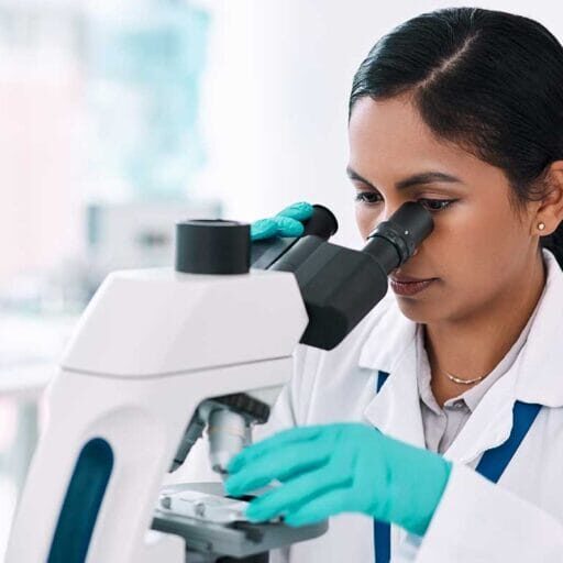 An internationally educated female healthcare professional working in a laboratory looking through a microscope