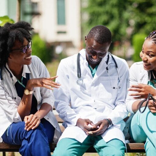 Three African American group doctors with stethoscope wearing lab coat sitting on bench.