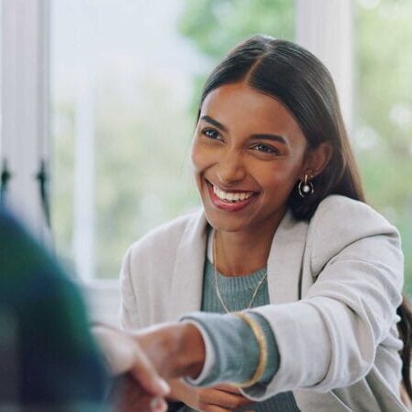 A female newcomer smiling and wearing business attire while shaking hands with an employer