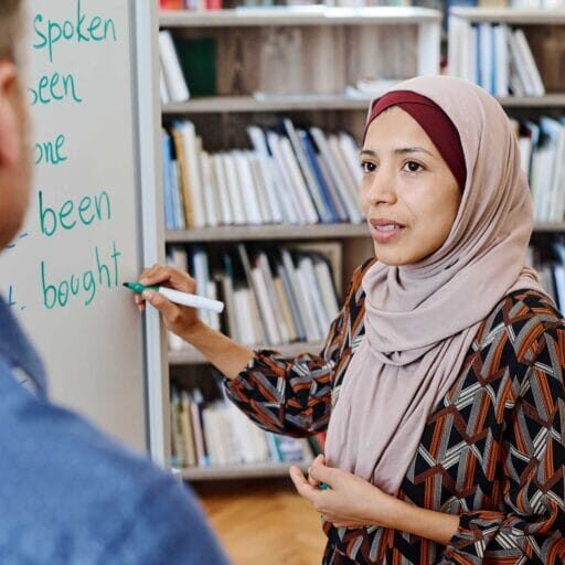 A muslim woman writing english on a white board and learning from an instructor
