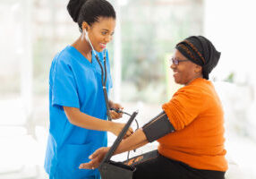 smiling african nurse checking senior patient's blood pressure