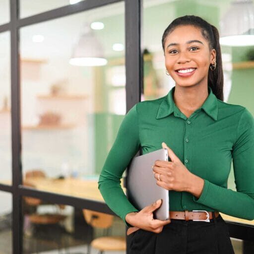 A skilled immigrant smiling in the office holding a laptop