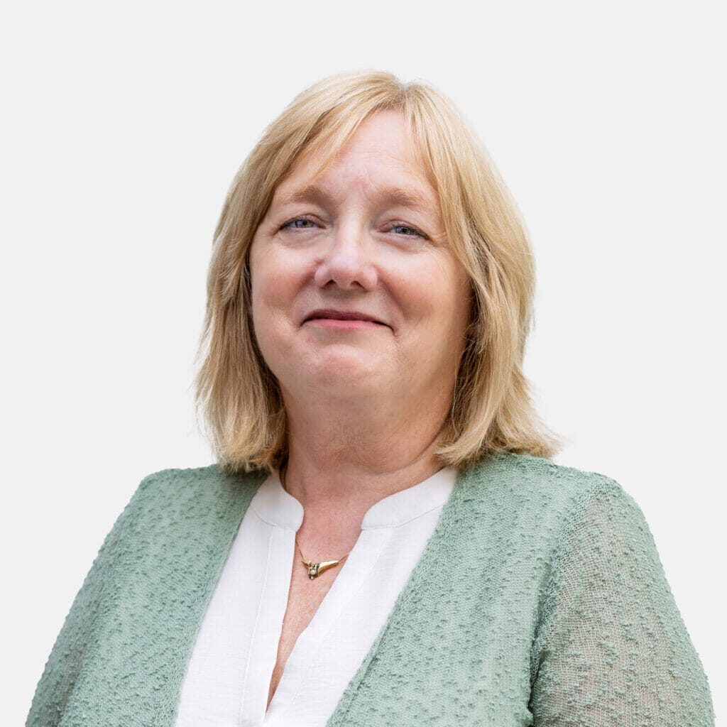Portrait of a smiling woman with blonde hair wearing a white blouse and a mint-green cardigan.
