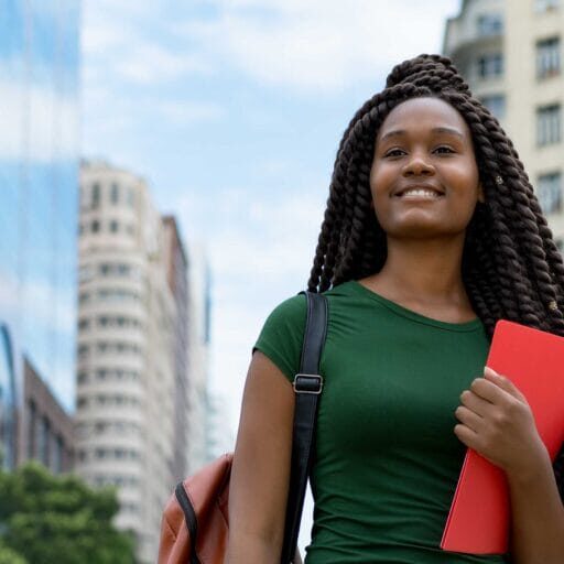A female refugee youth smiling in the city carrying a bag and a folder