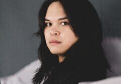 A portrait of Excel Garay, an artist. She has black hair wearing black clothe looking towards the camera while standing sideways.