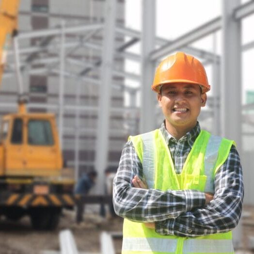 A male immigrant construction worker smiling in front of construction site